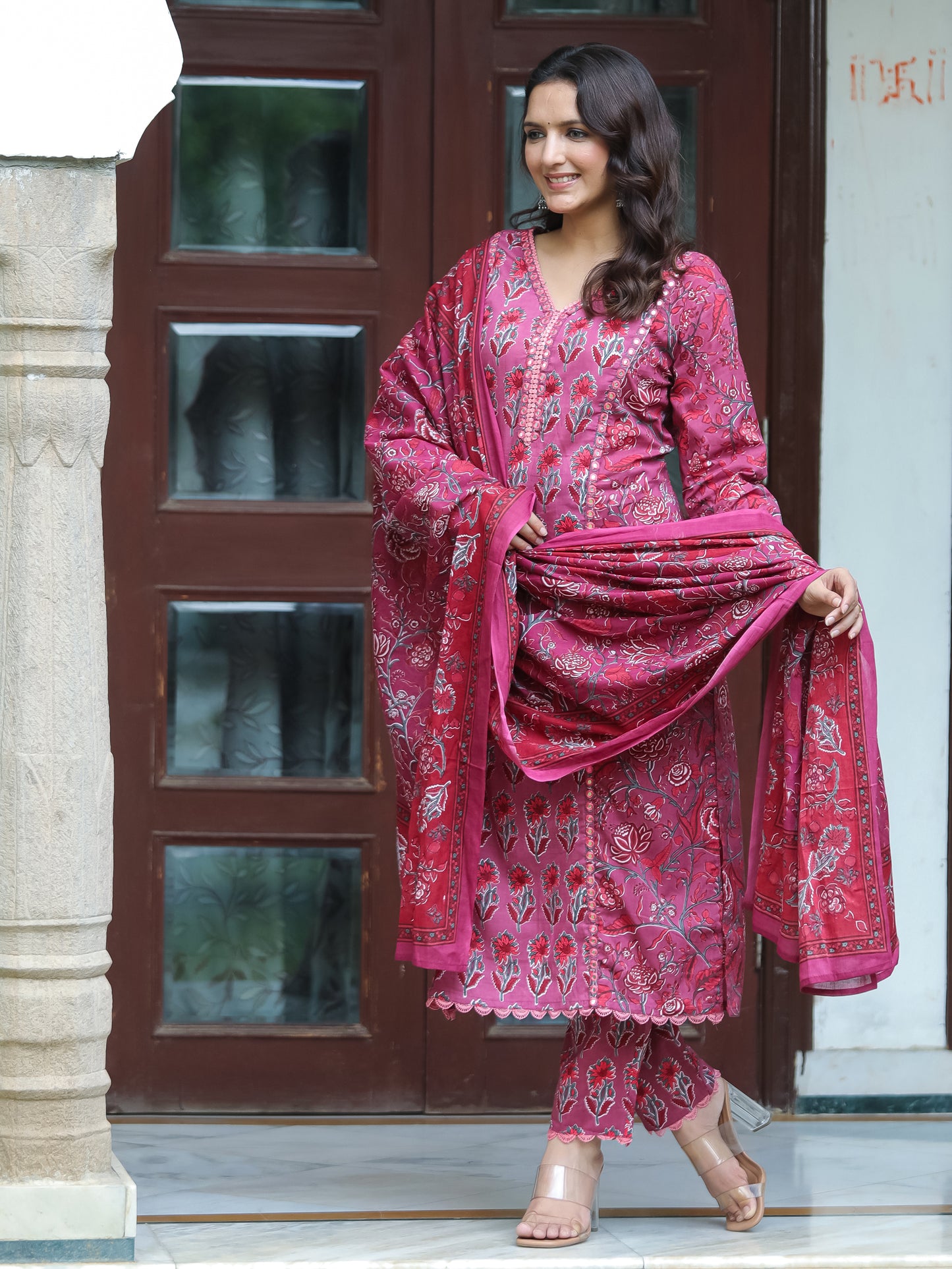 Flat lay of the Dark Fuschia Mirror Work Cotton Suit by Cottons Daily, featuring the V-neck straight-cut top with mirror and lace embellishments, floral printed straight-fit pants with lace work, and a matching floral printed dupatta, all crafted from soft cotton fabric.
