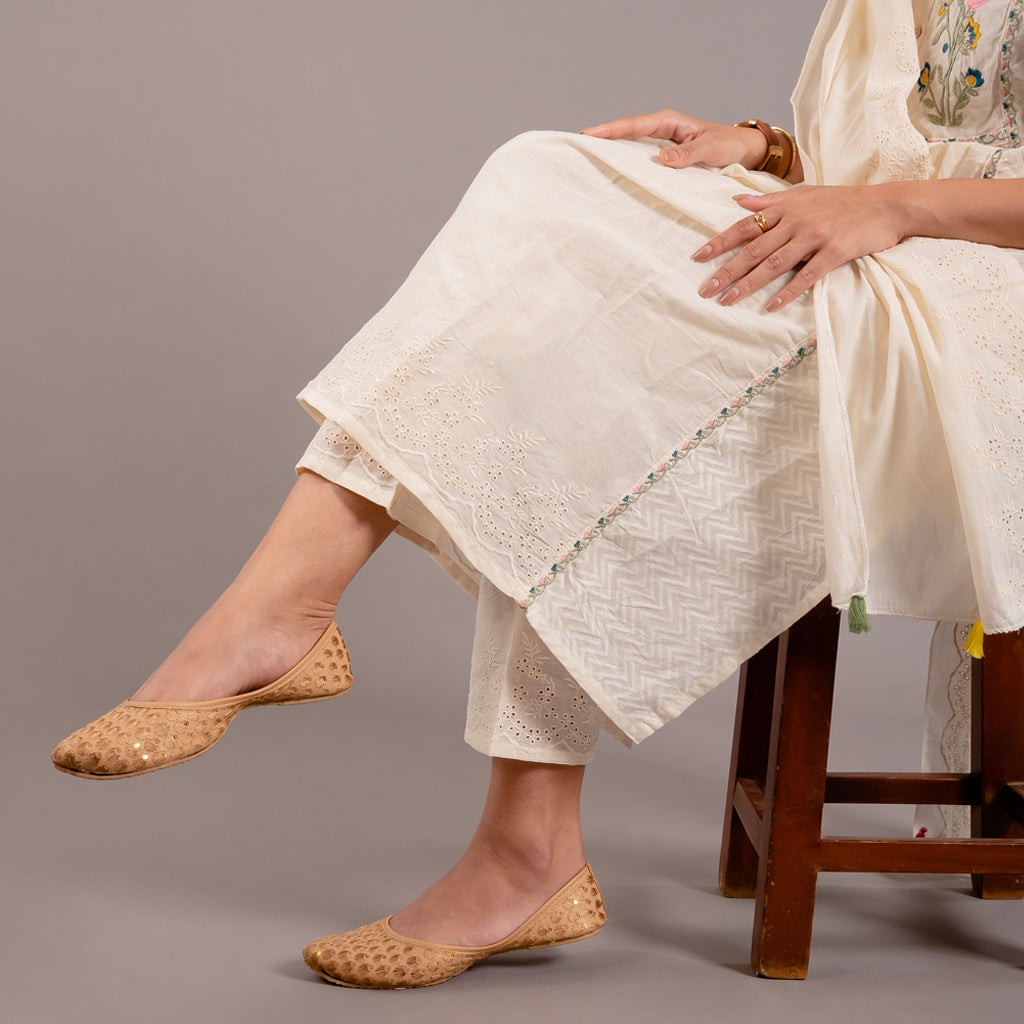 Model sitting gracefully on the chair showcasing the intricate designs on the kurta and the pant bottom of the Off White Floral Cotton Suit from Cottons Daily.