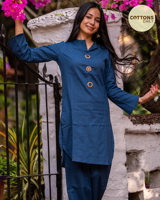 Front View: Navy Blue Solid Cotton Co-ord Set from Cottons Daily, showcasing a pure cotton top with a mandarin neckline, side slit cut, and subtle embellishments, paired with matching straight pants wore by a women, smiling and holding flowers in her hand.